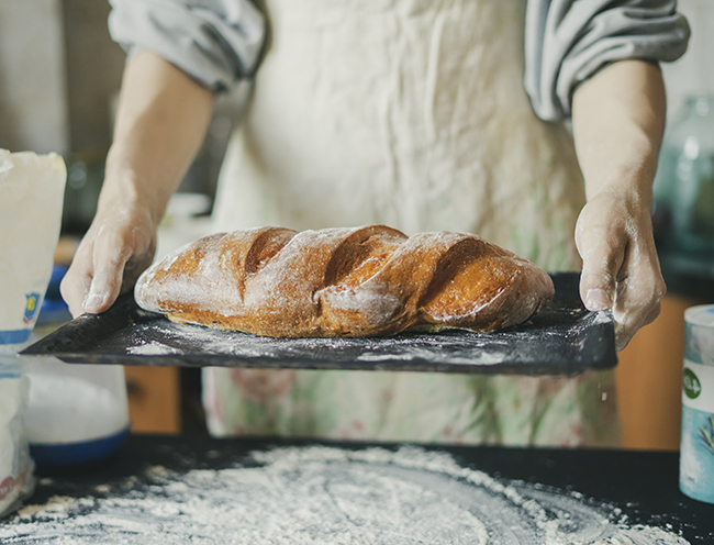 baker hands holding freshly cooked long loaf bread